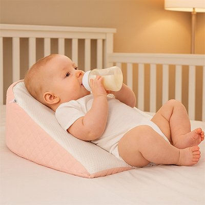 Bébé souriant confortablement installé sur cale incliné rose