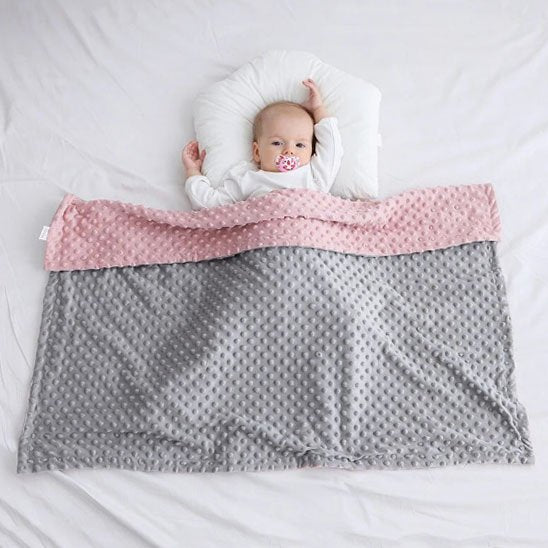 Nouveau-né allongé sur une couverture bébé tricot rose et grise personnalisée avec prénom brodé