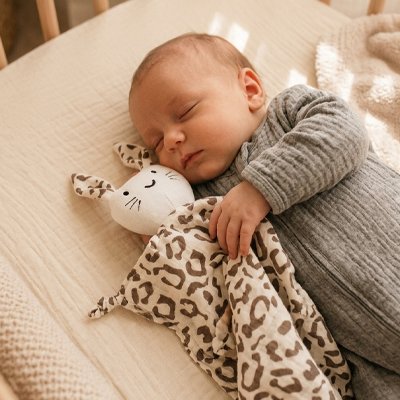 Nouveau-né endormi serrant un doudou lapin motif léopard, idéal cadeau naissance garçon ou fille