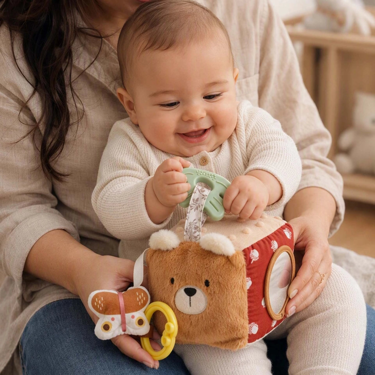 Maman qui tient son bébé souriant pendant qu'il manipule un cube d'éveil en tissu
